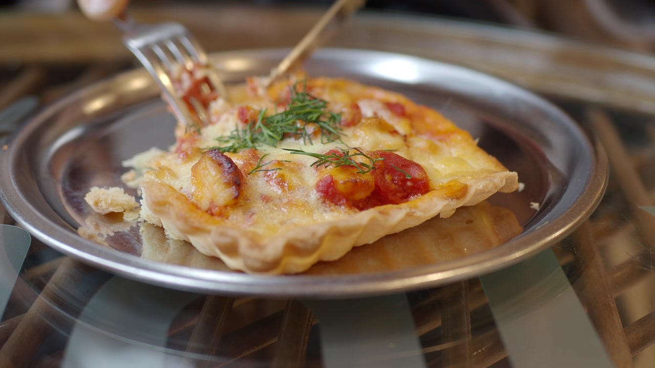 Close-up of a Person Cutting a Savory Quiche with Fork and Knife