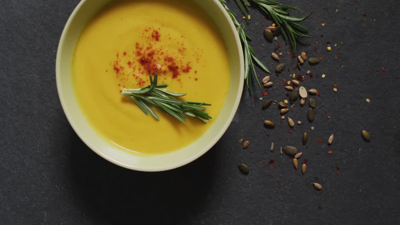 Video of cream vegetable soup in bowl on grey table with rosemary