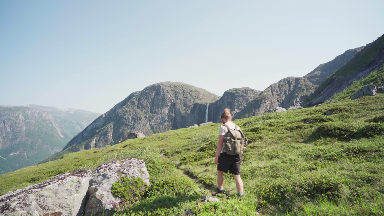 joven caminando sobre prados en las montañas con cascada mardalsfossen en noruega