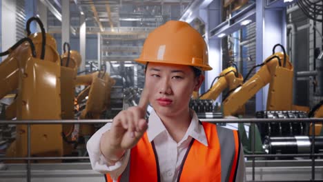 close up of asian female engineer with safety helmet disapproving with no index finger sign while standing with industrial robotic arms working