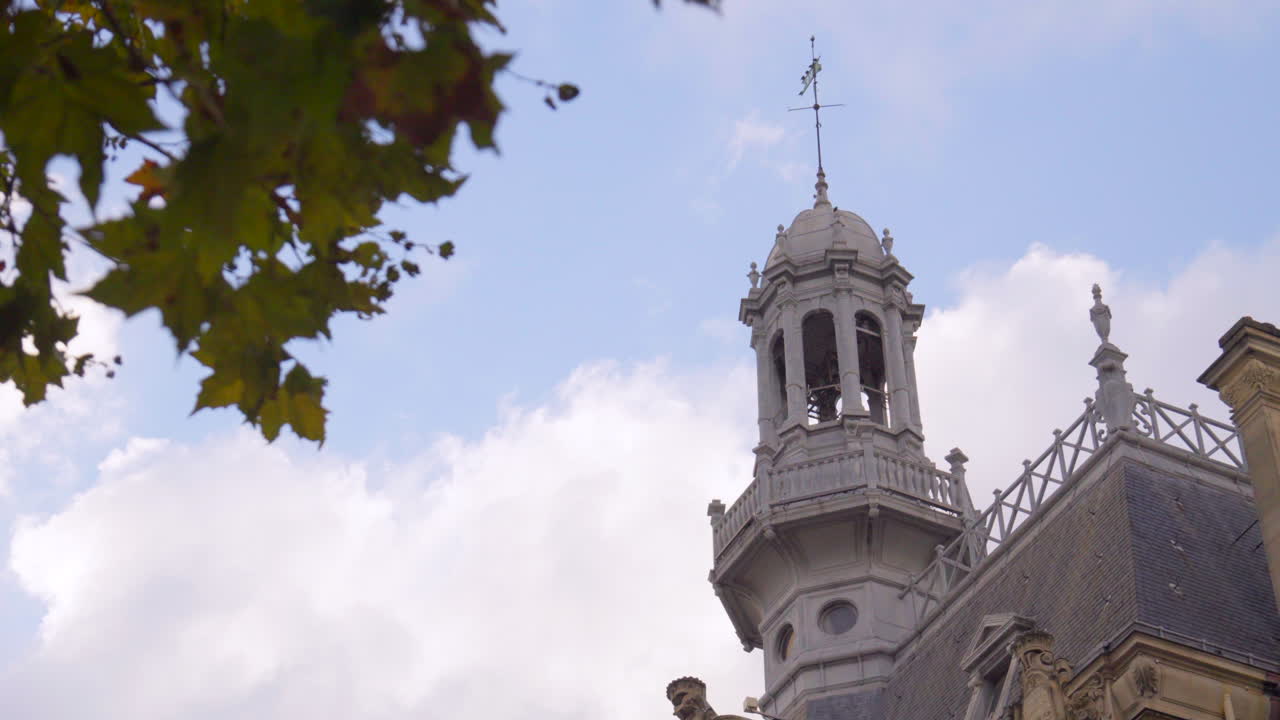 Una vista della torre e della banderuola sull'Hôtel de Ville di Asnières-sur-Seine, con parte del cielo visibile e foglie autunnali in primo piano, che creano una sfocatura morbida.