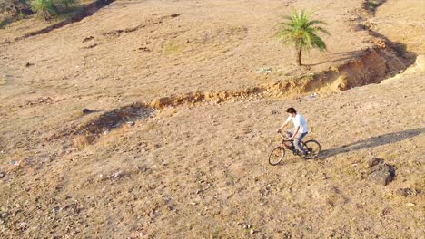 Luftaufnahme-Eines-Indischen-Mountainbikers,-Der-Versucht,-Einen-Stunt-Auszuführen-Und-Sich-Vom-Berg-Herunterbewegt