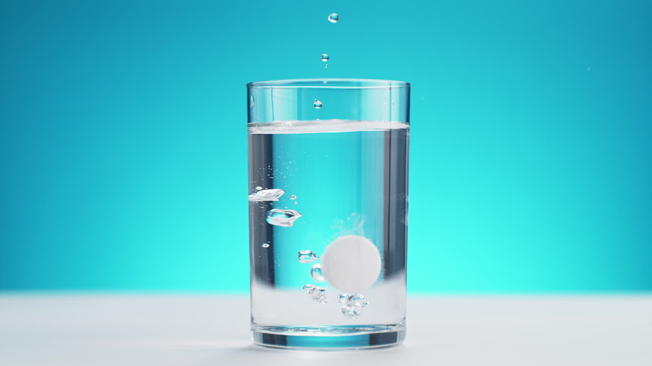 파란색 배경에 느린 동작으로 스플래시를 만드는 물 한 잔에 떨어지는 걱거리는 태블릿