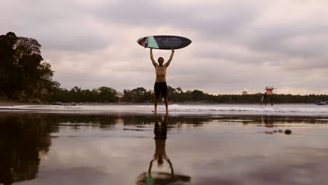 man holding surfboard at beach sunset