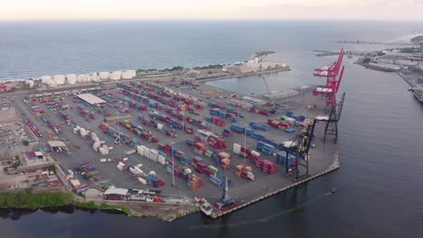 Circling-around-Port-Haina-during-sunset-shipping-containers-stacked-up-and-cranes-closed-no-boats-on-the-river-drone-aerial