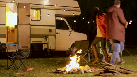 group of close friends dancing around camp fire in a cold night of autumn