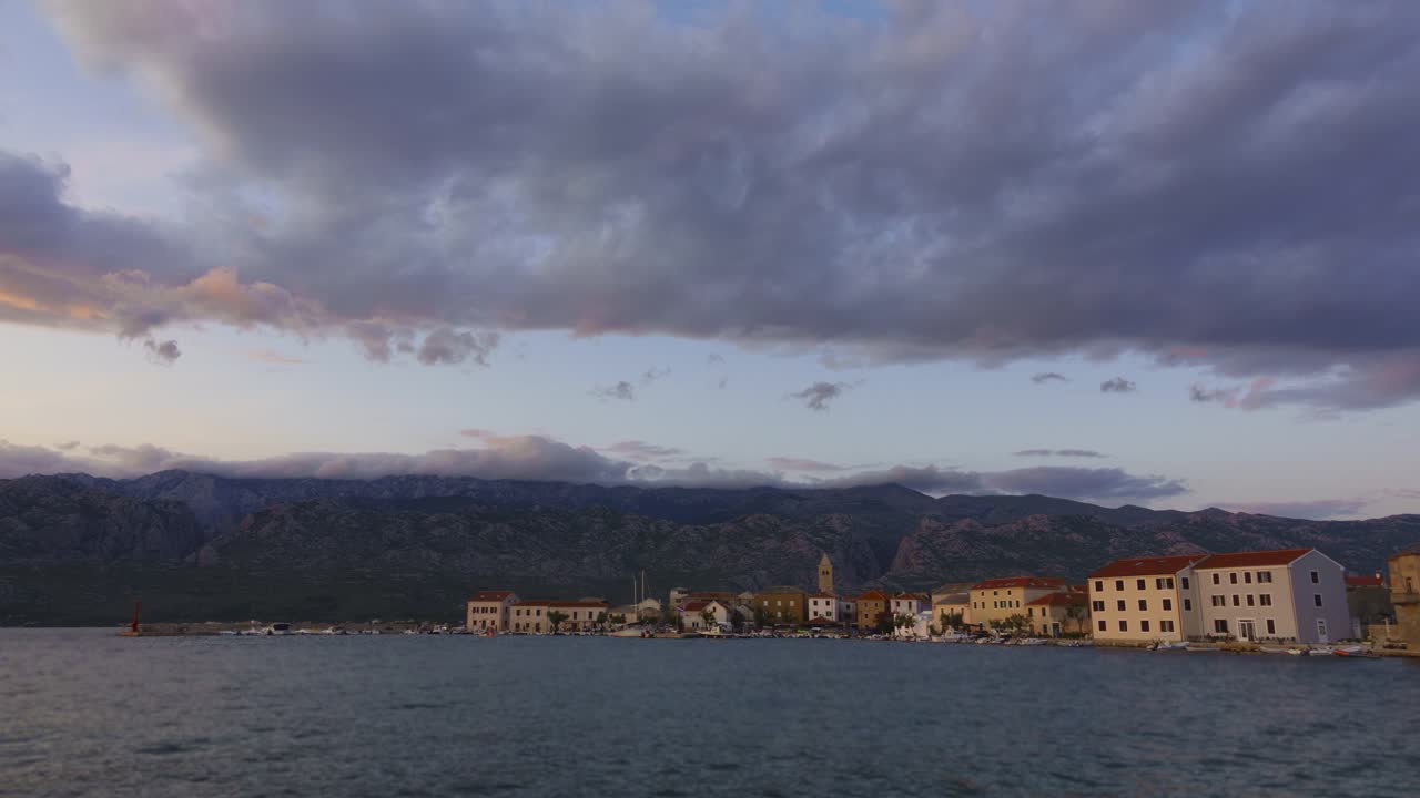 Day to night timelapse of small coastal town and harbor, mountains and rolling clouds in the background, colorful sunset in Dalmatian town Vinjerac, Croatia