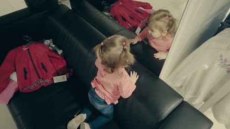 little-child-girl-in-a-clothing-store-sits-on-the-couch-in-front-of-a-mirror