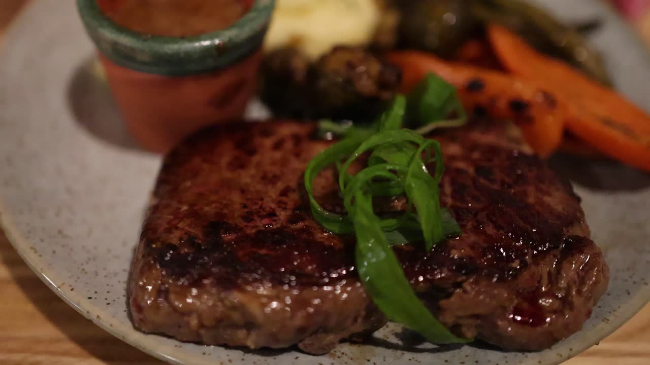 Camera slowly pans across juicy grilled steak, roasted carrots, green beans, and mashed potatoes