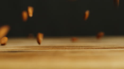 fotografía de cerca de nueces de almendra cayendo sobre una superficie de madera contra un fondo de estudio negro tomada en cámara lenta 3