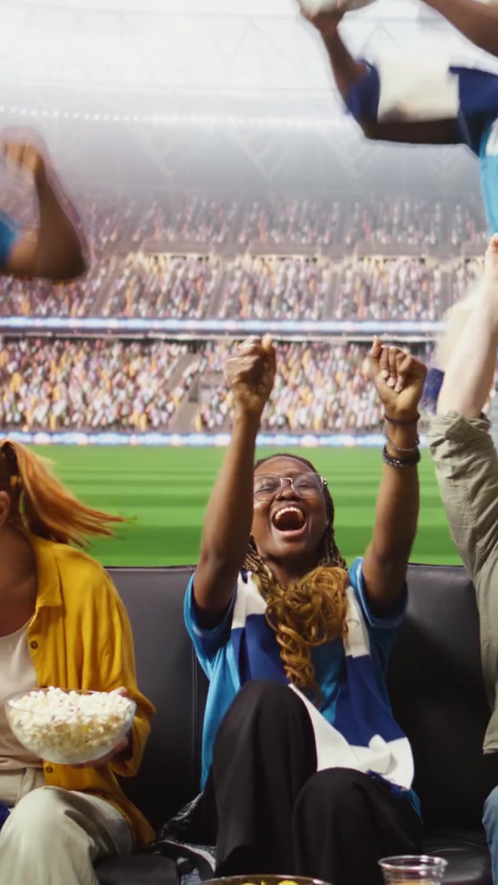 Video vertical: Aficionados al fútbol alegres en el sofá celebran un gol, sintiéndose como si estuvieran dentro del estadio