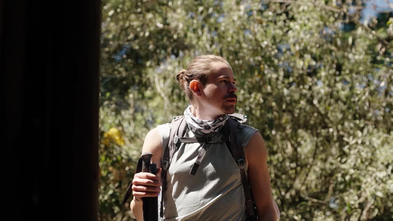 Focused hiker pauses during the Acatenango Volcano trek in Guatemala, holding trekking pole under warm forest light