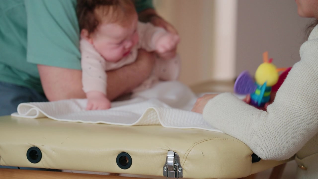 Close up view of the infant's head and upper body leaning forward, supported by an adult's forearm under the chest