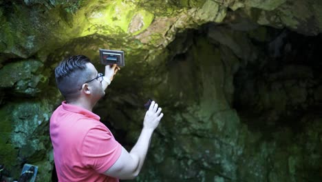 holding up a recorder, a man is recording some environmental ambient sounds in front of a cave known as the location of the tomb of the egyptian goddess bastet at strandzha mountain in bulgaria