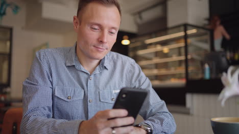 medium shot of young man wearing streetwear sitting in restaurant or cafe in front of laptop and having mobile phone. breakfast with smartphone