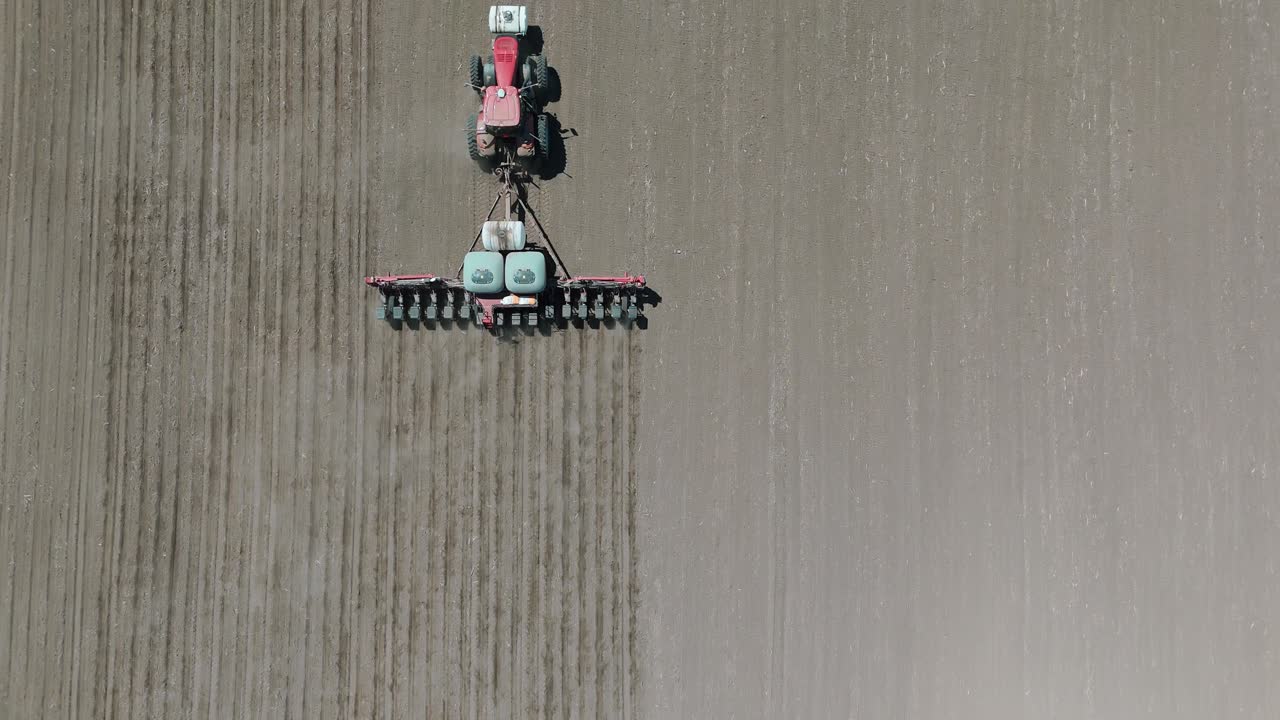 Drone footage of a farmer planting corn seeds in an iowa field in a red tractor