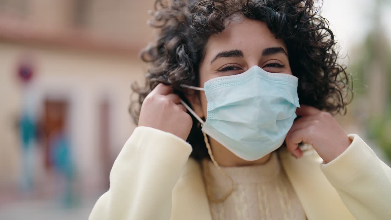 mujer joven sonriendo confiada usando máscara médica en la calle