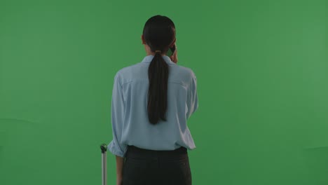 back view asian woman traveler with luggage talking on smartphone while standing in the green screen background studio, during sunset time