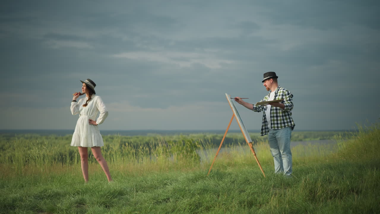 색 드레스와 모자를 입은 아름다운 여성이 색 셔츠, 청바지, 모자를 입고 있는 예술가 앞에 서 있습니다.