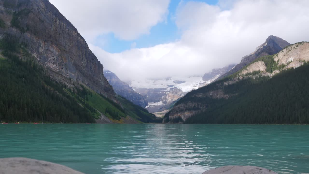 vista panorámica del lago louise, uno de los lagos más famosos del parque nacional de banff, alberta, canadá, en verano durante el día después de llover con nubes en el cielo y gente en canoa en el lago