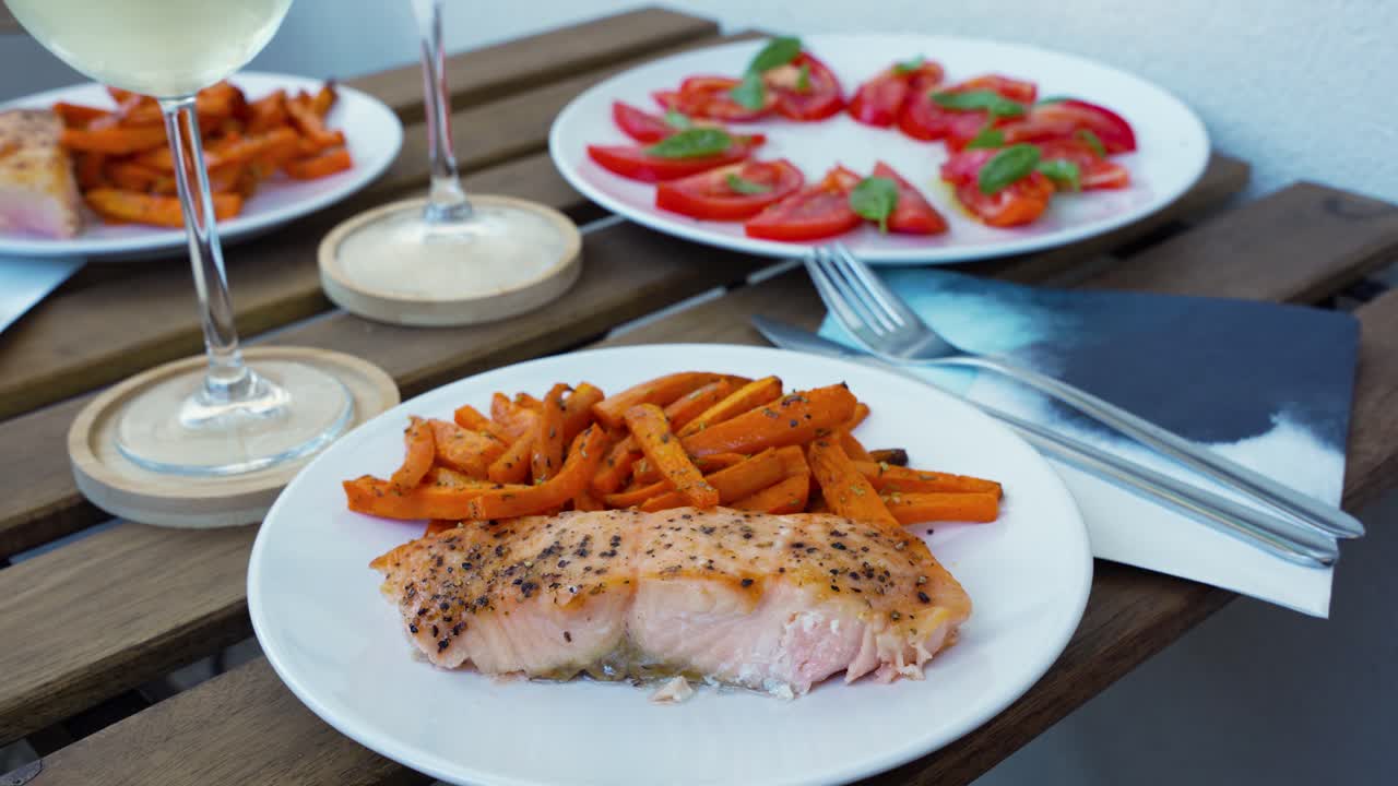 Grilled Salmon With Roasted Carrots And Tomato-Basil Salad On Plates Served With Glasses Of White Wine On Wooden Table For Dinner. closeup shot