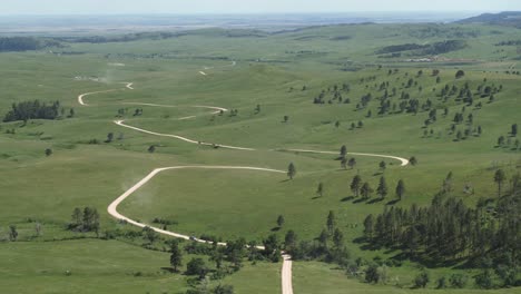 Aerial,-cars-on-road-trip-driving-on-long-winding-road-in-green-nature-park-with-vast-green-grass-fields