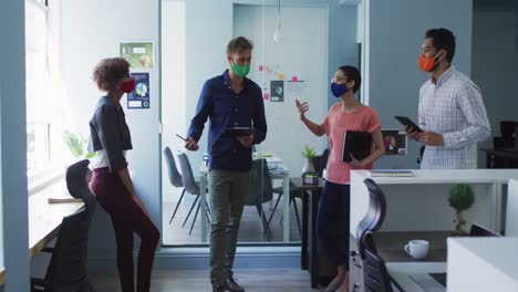 Portrait-of-diverse-colleagues-wearing-face-masks-discussing-together-at-modern-office