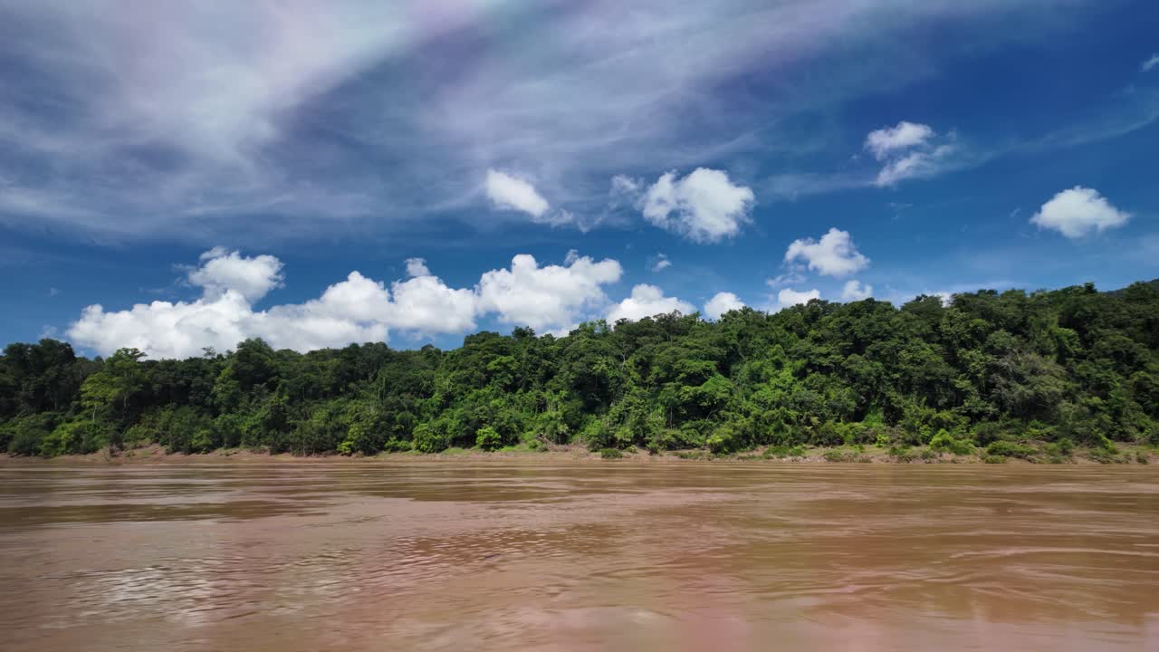 Mekong River scene in Laos showing muddy water, dense tropical forest, and a clear blue sky