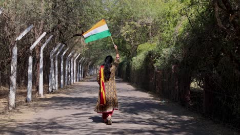 young girl walking with the indian tricolor national flag at remote location at day from back angle