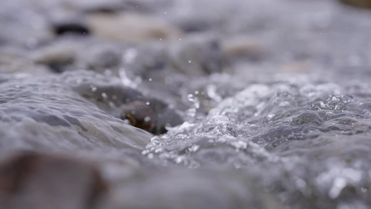 Acqua fresca scorre impetuosa su rocce scure con flusso turbolento, bolle e schizzi in Islanda, catturata come un macro primissimo piano con una telecamera statica
