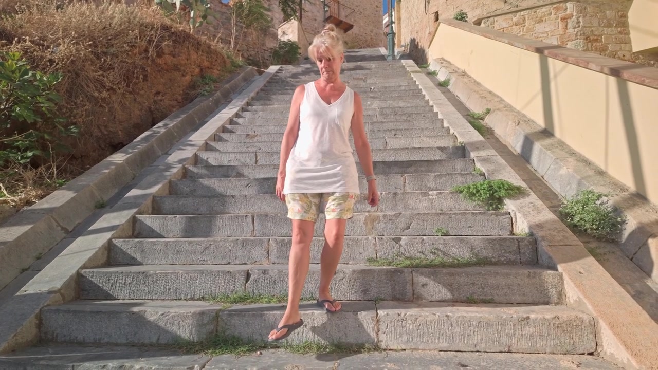 Donna che scende con cautela ripidi gradini di pietra in una località turistica greca.