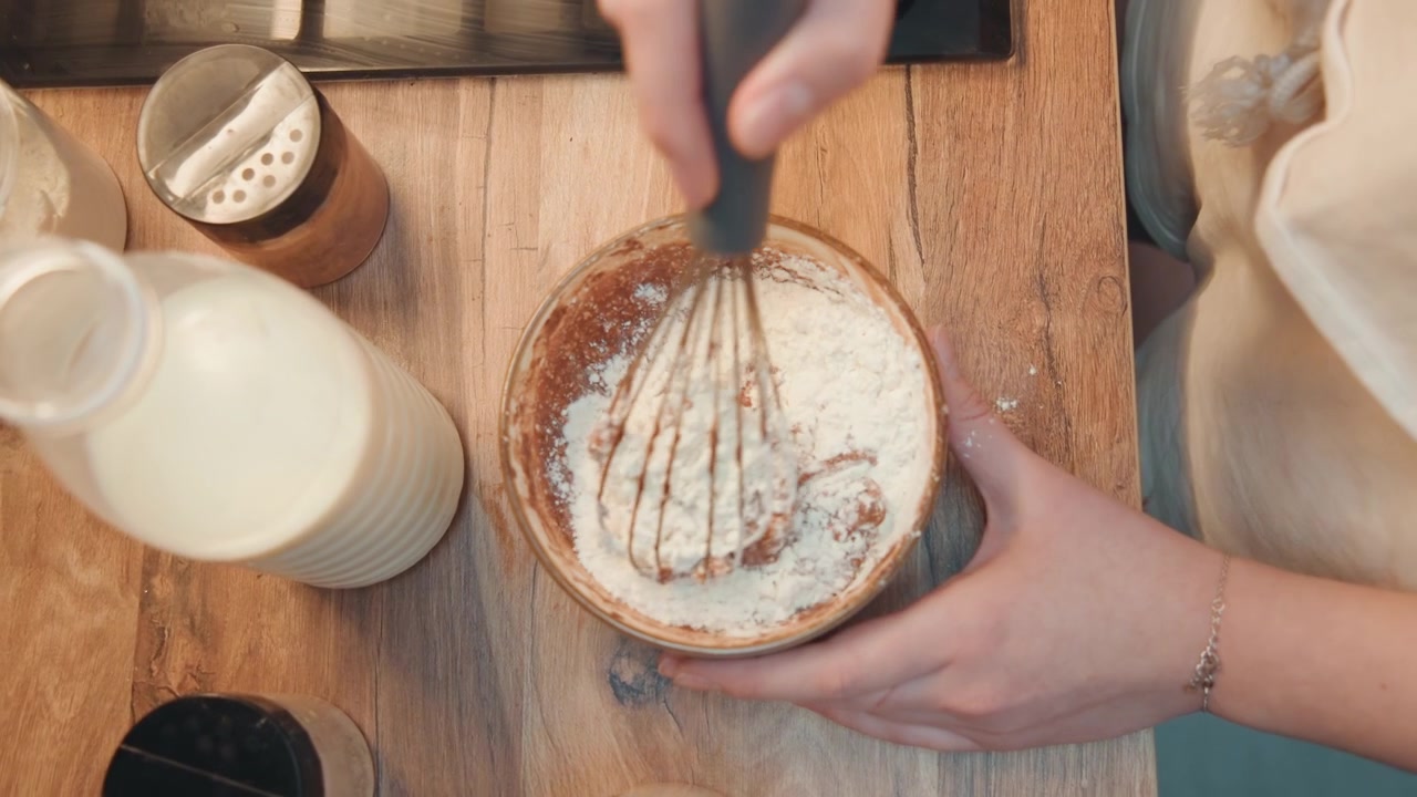 Ovenfra-bilde av hender som drysser melis over bakverk, melkeflaske og glass på et trebrett, stylingrekvisitter for en frokostfotografering, varmt morgenlys, hjemmelaget matscene med matblogger-styling.