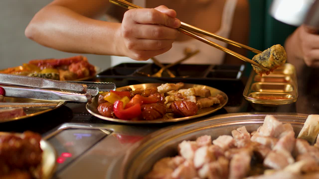 Woman uses chopsticks to dip grilled meat in sauce at lively indoor barbecue restaurant