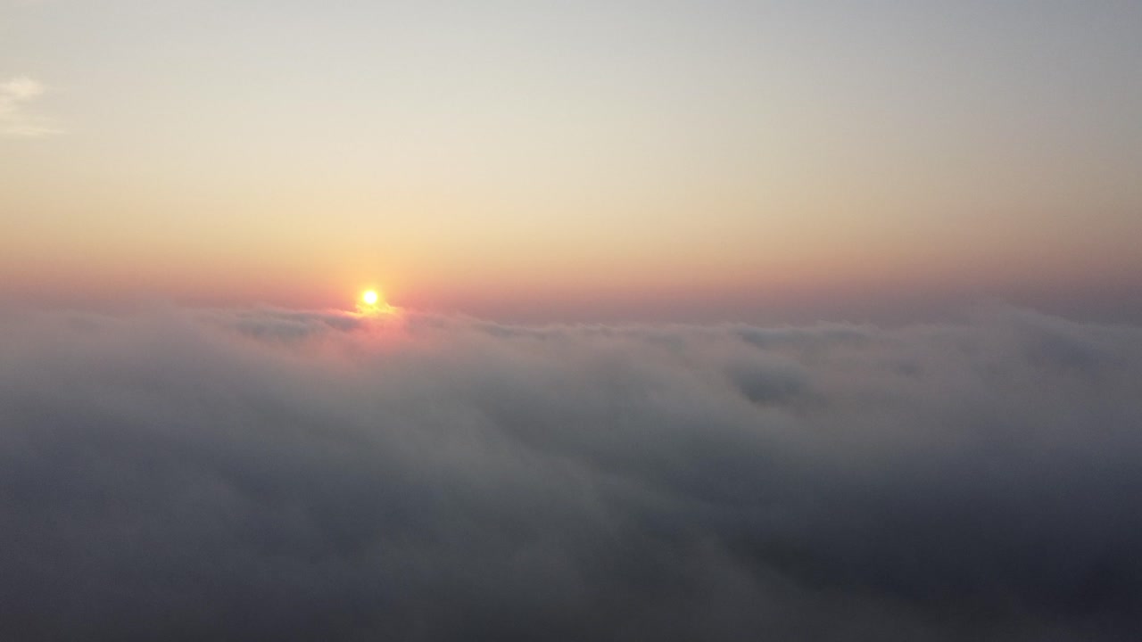 Aerial ascend above cloud level revealing early morning sunrise in sky; 4k