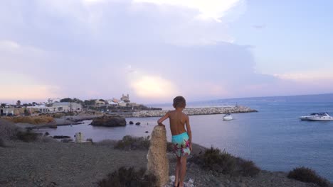 boy is leaning on the rock and watching over the shore of spanish island