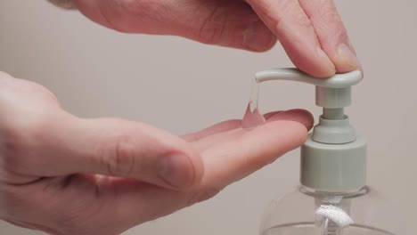 Close-up-of-male-hands-pushing-on-a-dispenser-with-liquid-transparent-soap-to-wash-hands-on-a-white-background