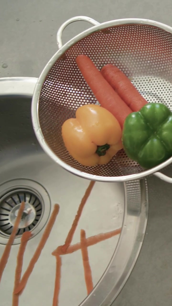 Vertical video: Peeling carrot, hands with blue cuff grasping peeler at kitchen sink for cooking