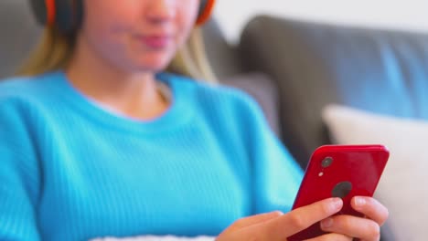 primer plano de una adolescente sentada en el sofá con auriculares inalámbricos transmitiendo contenido desde el teléfono móvil - filmado en cámara lenta
