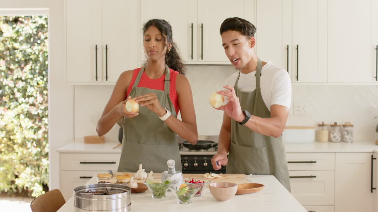 Starting prep in kitchen African American couple in olive aprons peeling, comparing onions, knife
