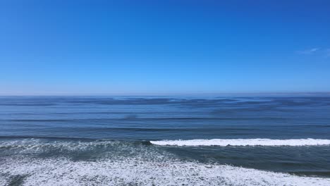 Eleva-Tus-Sentidos-Con-Esta-Impresionante-Toma-Aérea,-Que-Captura-Las-Fascinantes-Olas-Azules-Del-Océano-En-Perfecta-Transición-Hacia-El-Cielo-Azul-Claro.