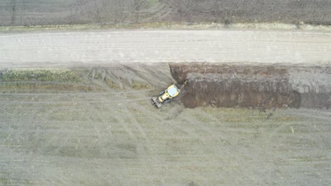 aerial top down ascend over tractor excavator dig drainage trench near road