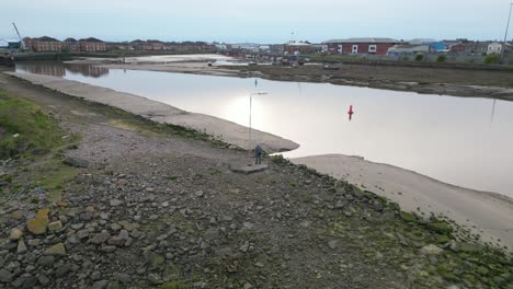 Einsamer-Mann-Mit-Einsamem-Laternenpfahl-Auf-Brachland-Neben-Dem-Fluss-An-Der-Flussmündung-Des-Flusses-Wyre,-Fleetwood,-Lancashire,-Großbritannien