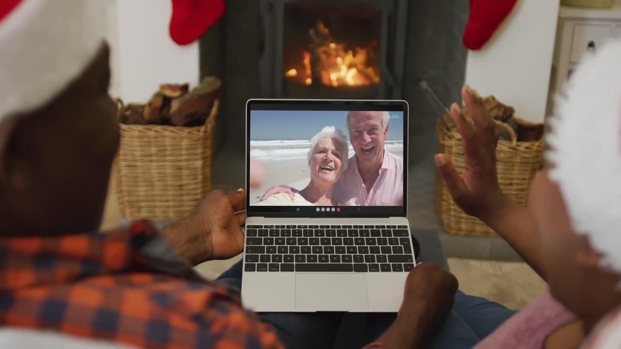 pareja afroamericana con sombreros de santa usando una computadora portátil para una videollamada de navidad con la pareja en la pantalla