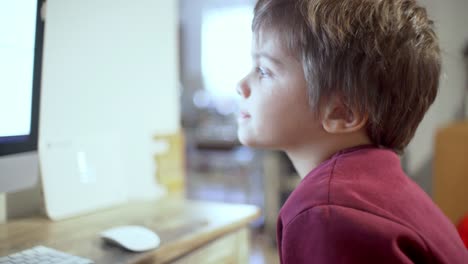 Pan-close-up-shot-of-caucasian-boy,-watching-a-computer-screen-for-distance-education-purposes,-during-coronavirus-lockdown-4K