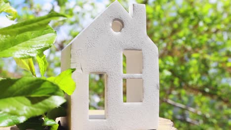 a beautiful model of a house on a wooden surface with lush green plants and a blue sky in the background.