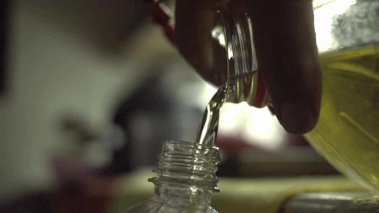 Close up of cooking oil pouring into a plastic bottle, highlighting ingredient transfer, liquid flow and food preparation activities in an indoor kitchen setting.