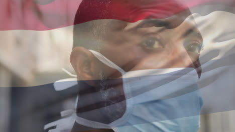 animation of waving netherlands flag against african american man in face mask on the street