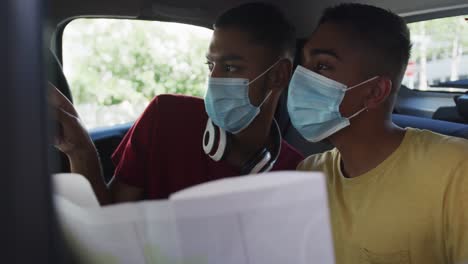 two mixed race male friends wearing face masks using map in cab