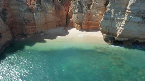 drone flying away from small beach, revealing tall cliffs and a stunning blue sea