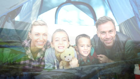 family camping in tent, smiling children holding teddy bear over natural landscape